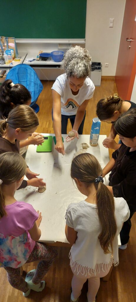 Kinder stehen um einen Tisch und backen gemeinsam Brot. 