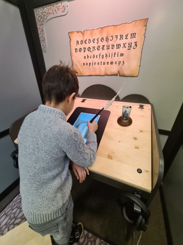 Ein Kind sitzt an einem Pult und schreibt Feder und Tinte. 