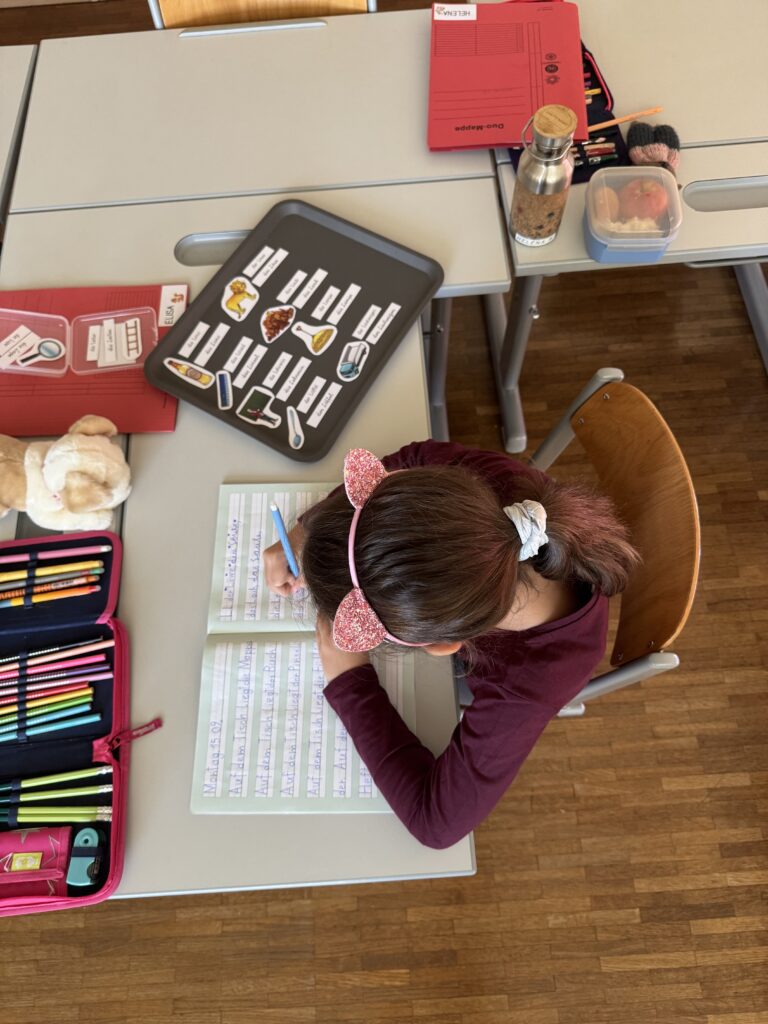 Ein Kind sitzt mit Freiarbeitsmaterial "Deutsch" und schreibt die Wörter in das Heft. 