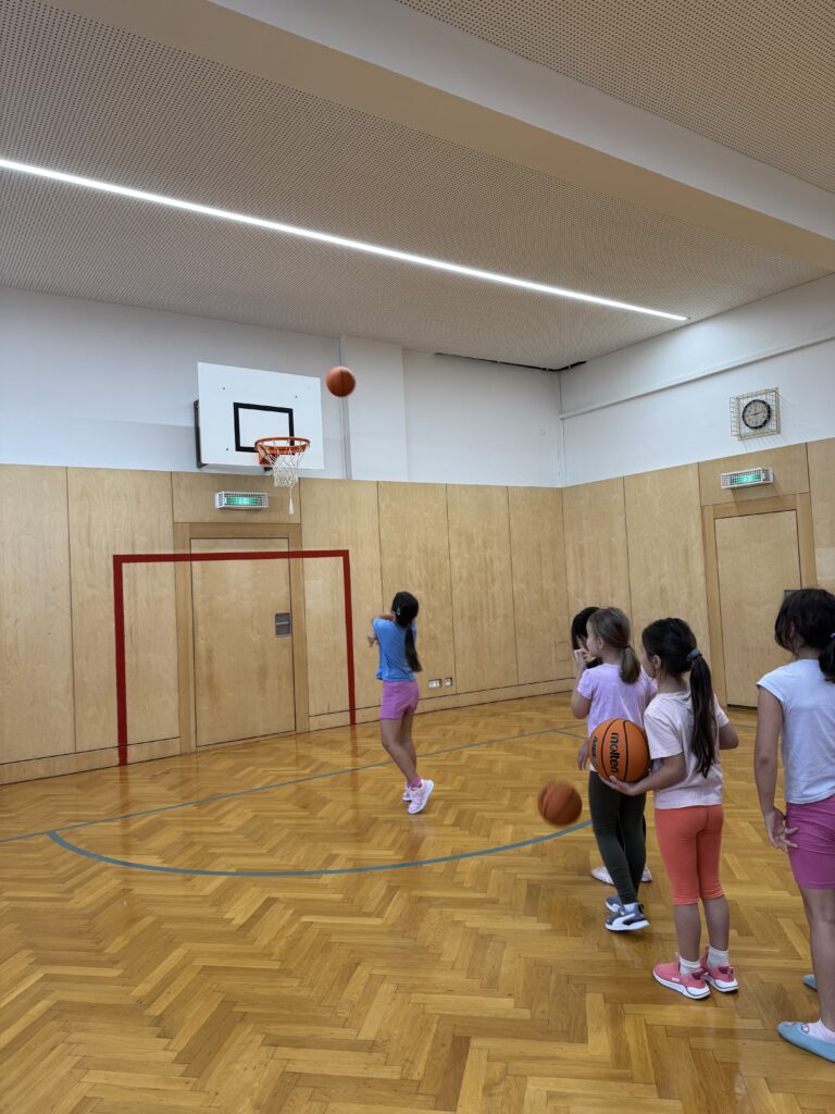 Im Turnsaal werfen Kinder die Bälle in den Korb. 