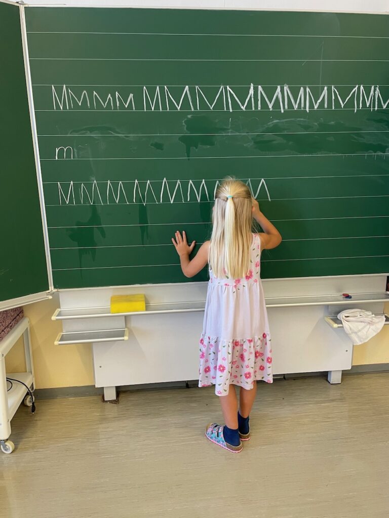 Ein Kind übt an der Tafel den Buchstaben "M". 