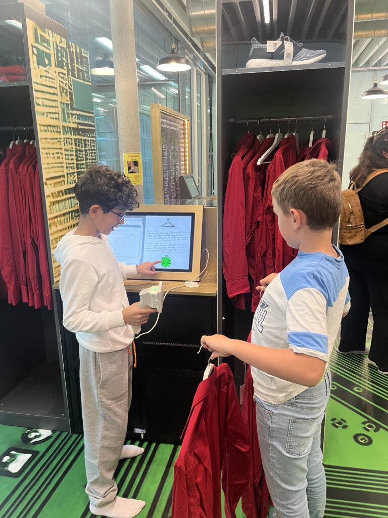 Ausstellung im Frida und Fred zum Thema: "Damals 1410". Zwei Kinder stehen sich gegenüber, einer hält ein rotes Hemd in der Hand.  