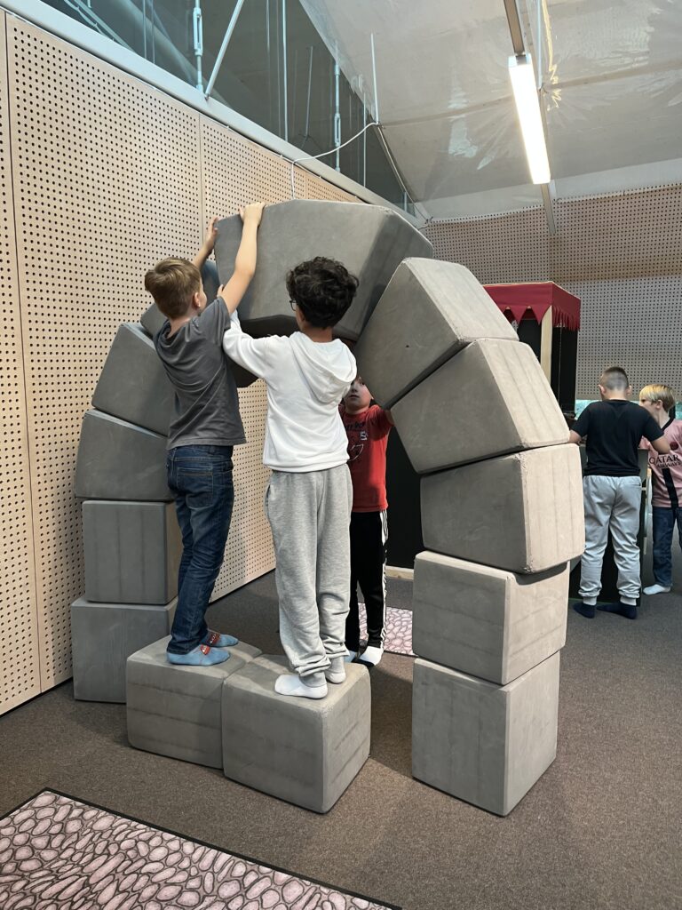 Ausstellung im Frida und Fred zum Thema: "Damals 1410". Zwei Kinder bauen ein Tor aus grauen großen Bausteinen. 