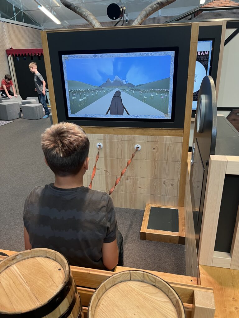 Ausstellung im Frida und Fred zum Thema: "Damals 1410". Ein Kind sitzt in einer Kutsche. Er führt die Kutsche über einen Bildschirm. 