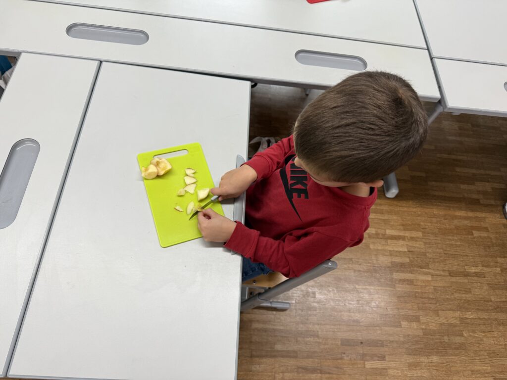 Wir backen einen Apfelkuchen: Ein Kind schneidet auf einem grünen Brett einen Apfel. 