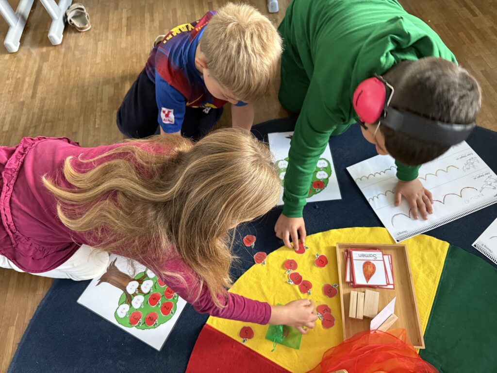 Drei Kinder lösen gemeinsam Rechenaufgaben im Zahlenraum 5. Dabei wird eine Apfelbaum mit Äpfel bestückt. 