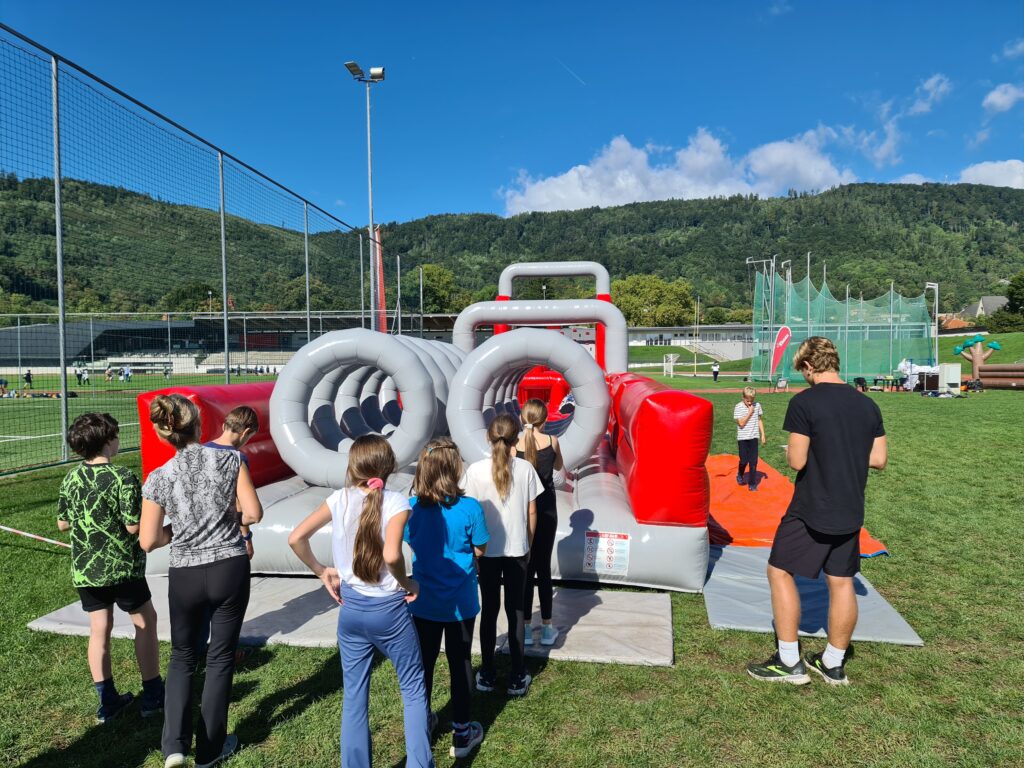Kinder beim Servus bewegt Kinder Aktionstag in Graz. Vier Kinder sehen vor dem großen Airtrack. 