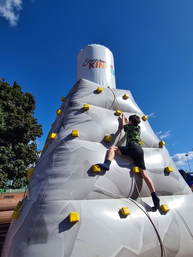 Kinder beim Servus bewegt Kinder Aktionstag in Graz. Ein Kind klettern auf den Kletterturm. 