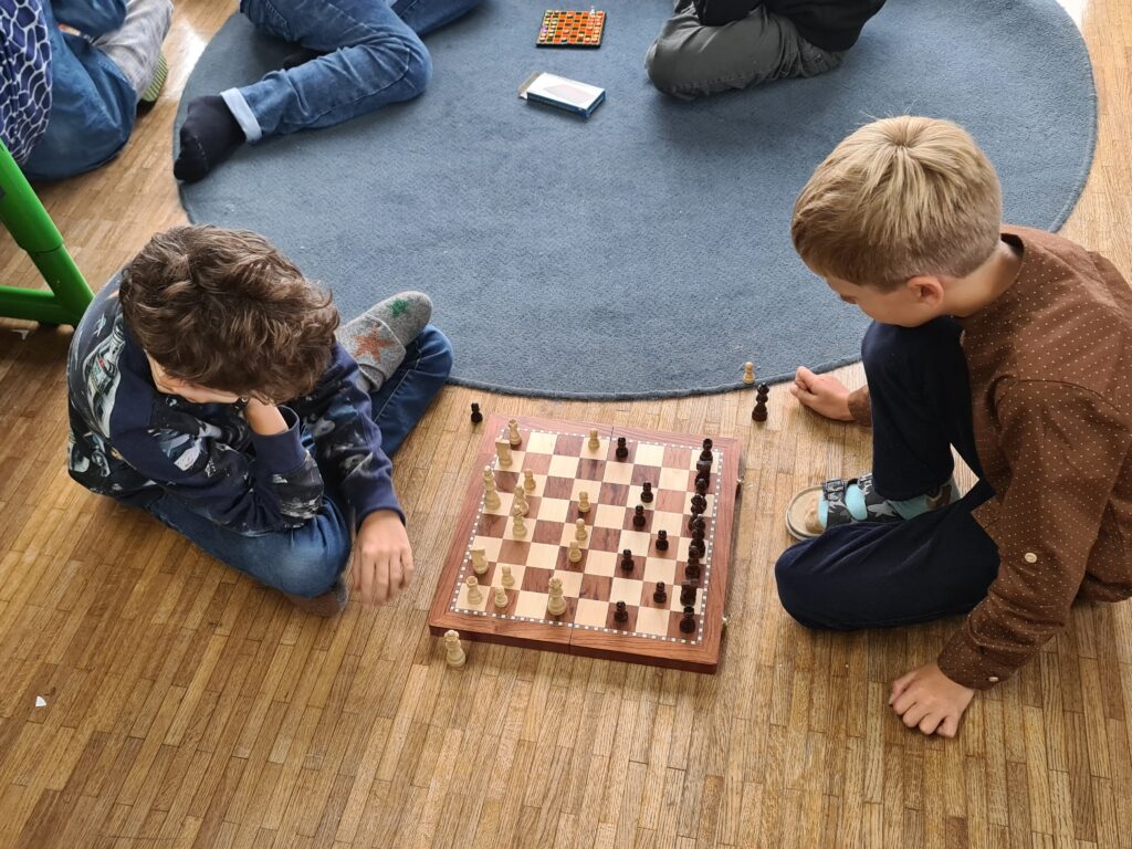 Zwei Kinder sitzen auf dem Boden und spielen in der Pause Schach. 