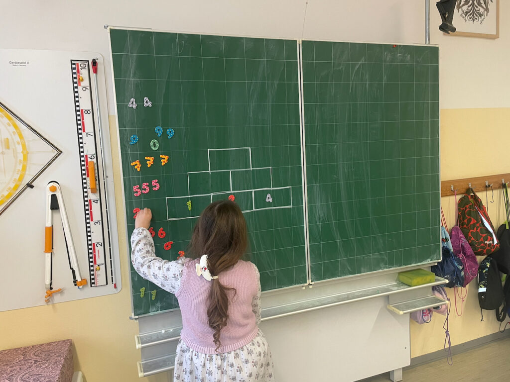 Ein Kind löst eine Rechenmauer an der Tafel.