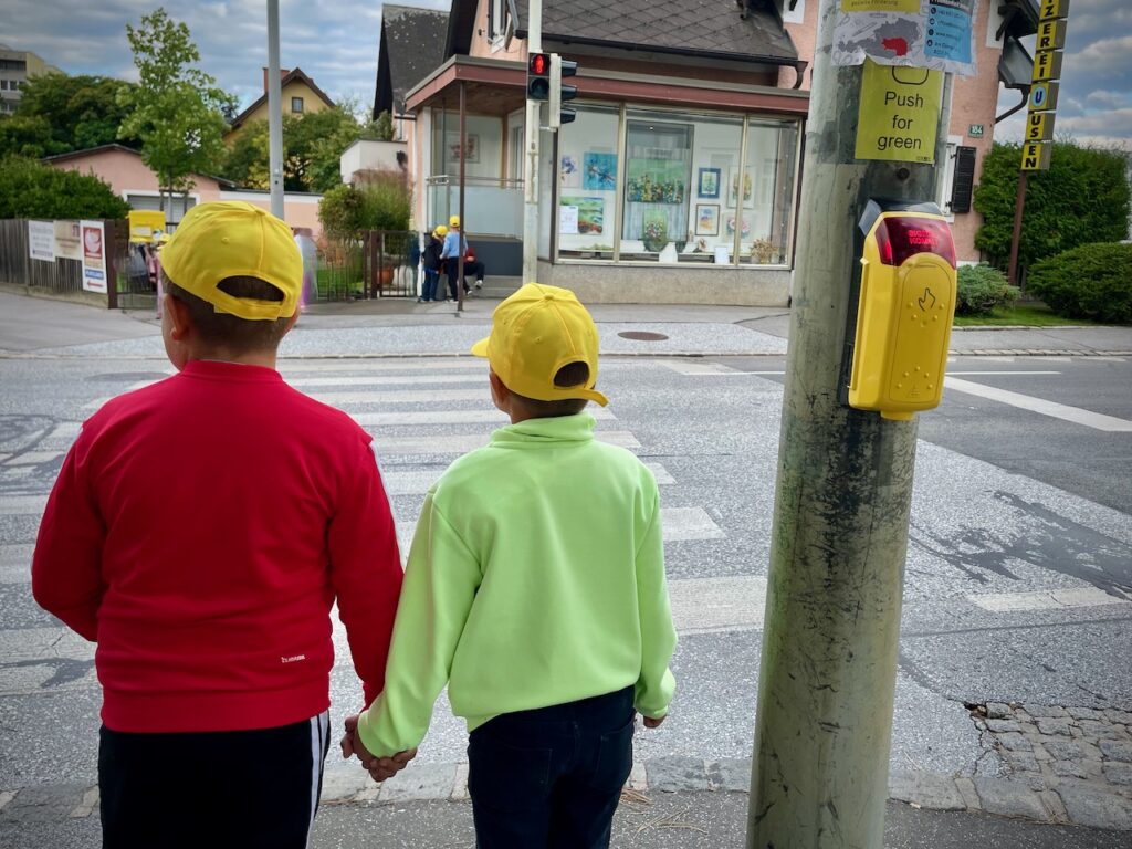 Verkehrssicherheit üben! Zwei Kinder stehen vor der Ampel und wollen den Zebrastreifen überqueren. 