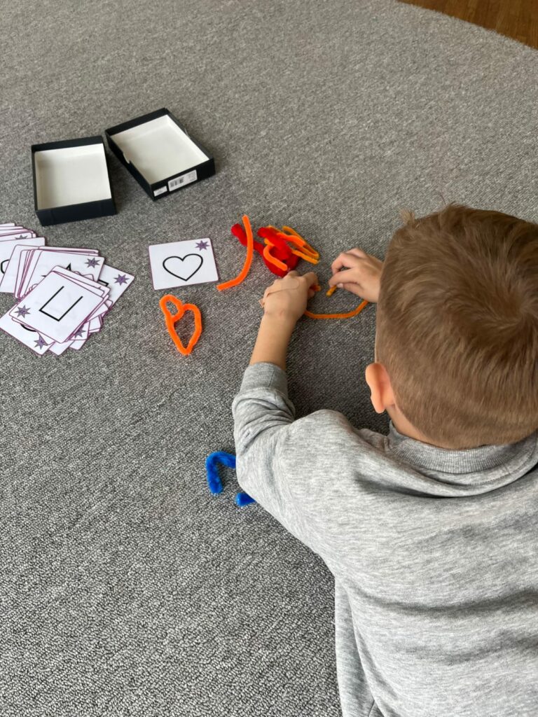 Ein Kind sitzt am Boden und formt mit bunten Pfeifenreiniger Formen nach. 