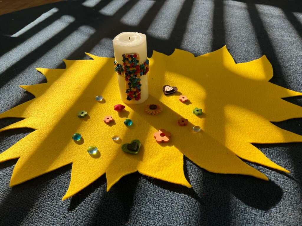 Auf dem Bild sieht man eine schön gestaltete Kerze rundherum liegen Blümchen und Steinchen. Kinder haben für den Religionsunterricht eine Klassenkerze gestaltet. 