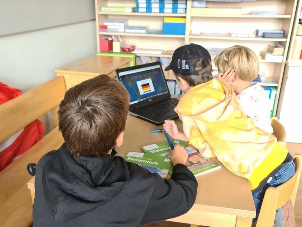 Kinder sitzen vor einem Laptop und recherchieren über verschiedene Themen. 