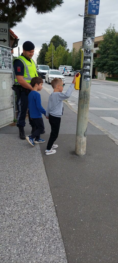 Verkehrserziehung: Zwei Kinder stehen mit einem Polizisten bei der Ampel.